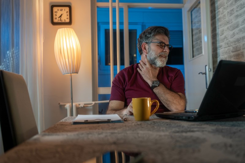 Osoba na zdjęciu wygląda na odczuwającą ból gardła w nocy. Może to być spowodowane suchością powietrza, alergiami lub refluksem żołądkowo-przełykowym. Pomocne mogą być nawilżacze powietrza, unikanie jedzenia przed snem oraz picie ciepłych napojów. W przypadku utrzymujących się objawów warto skonsultować się z lekarzem.