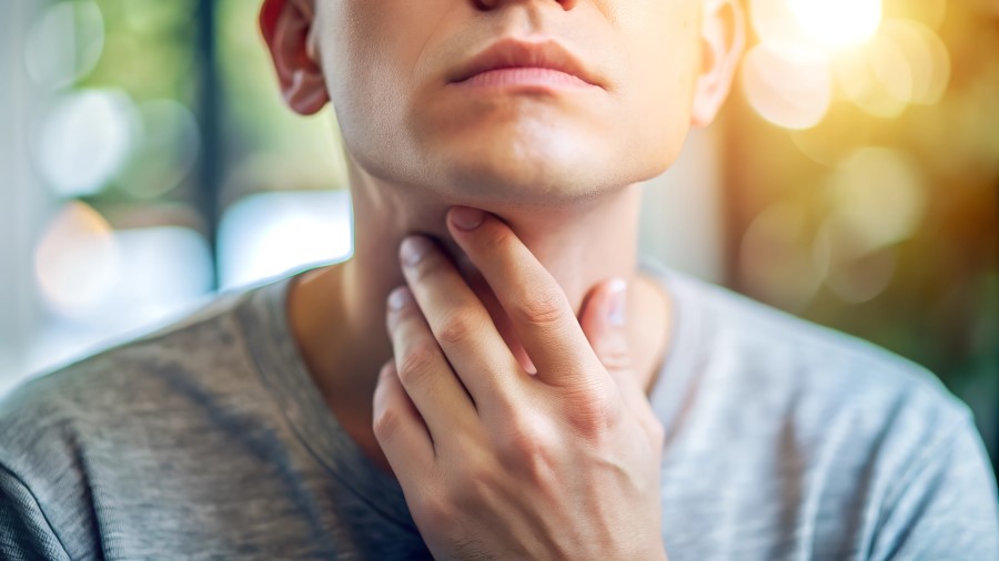 Osoba na zdjęciu trzyma się za gardło, co może sugerować grzybicę poantybiotykową. Jest to infekcja grzybicza, która może wystąpić po długotrwałym stosowaniu antybiotyków, osłabiających naturalną florę bakteryjną. Objawia się białawym nalotem, bólem i dyskomfortem w jamie ustnej lub gardle. Wymaga leczenia przeciwgrzybiczego i konsultacji z lekarzem.