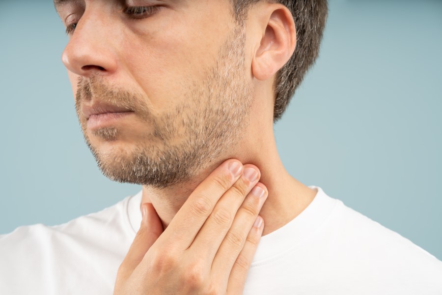 Osoba na zdjęciu trzyma się za gardło, co może sugerować nawracającą anginę. Nawracająca angina to częste zapalenie migdałków, które może powodować ból gardła, trudności w przełykaniu i obrzęk węzłów chłonnych. Wymaga konsultacji z lekarzem i może być leczona antybiotykami lub innymi metodami w zależności od przyczyny.